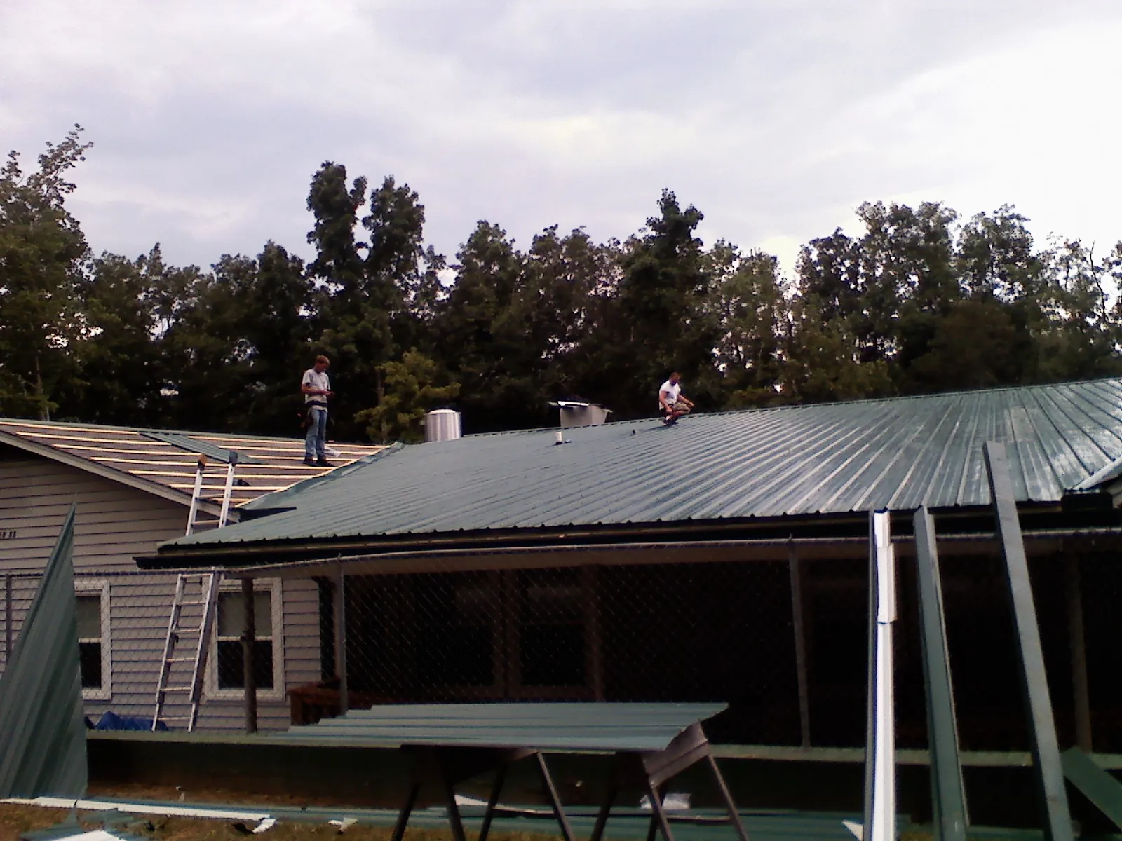 Two roofers installing green metal panels above a covered porch in Canaan